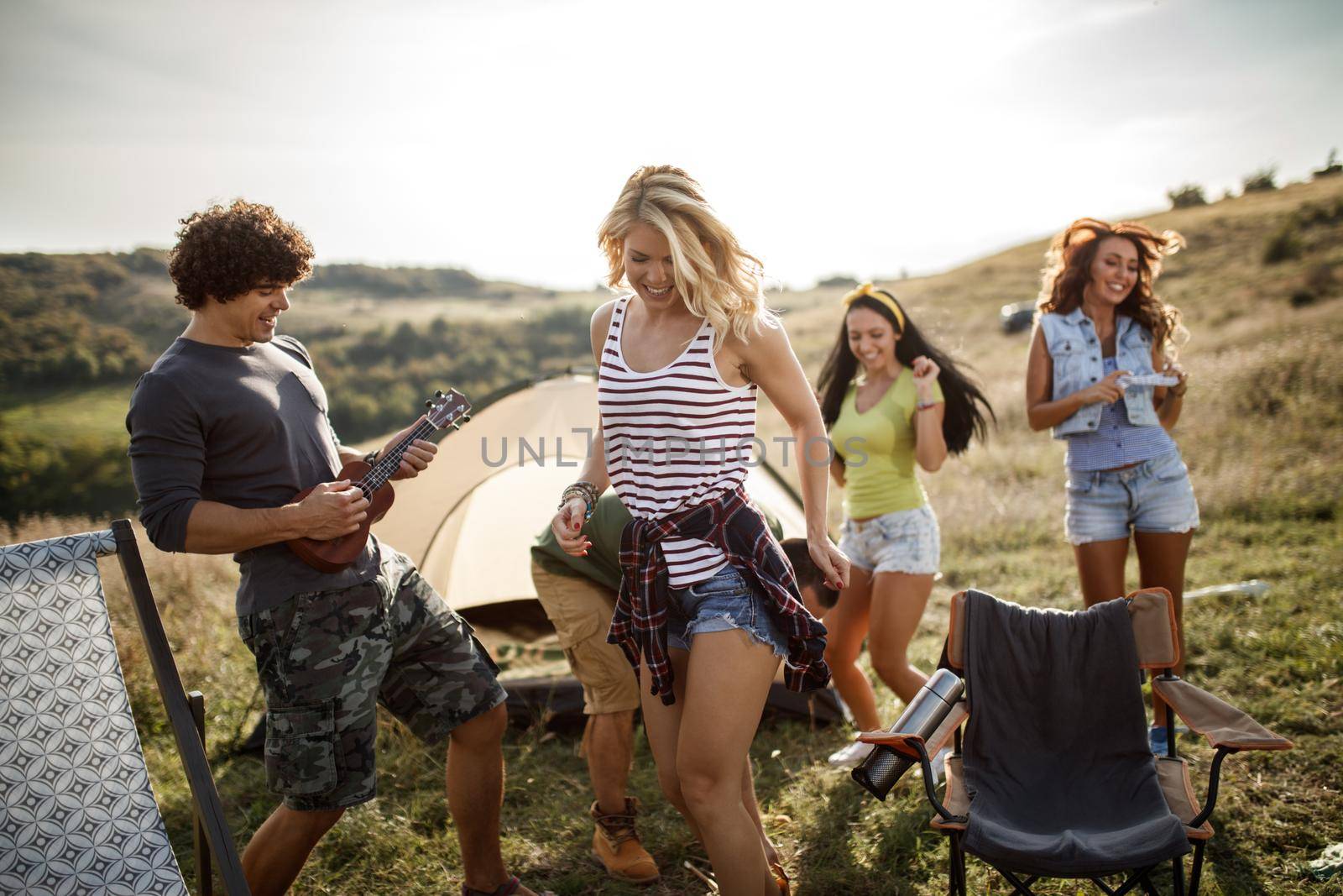 A group of cheerful friends having fun outside their tent at a festival.