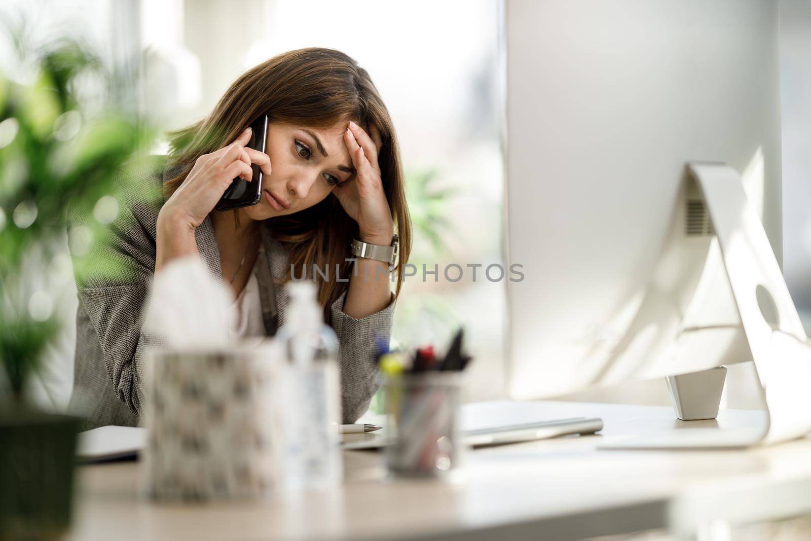 A tired business woman sitting alone in her home office and worriedly talking on smartphone.