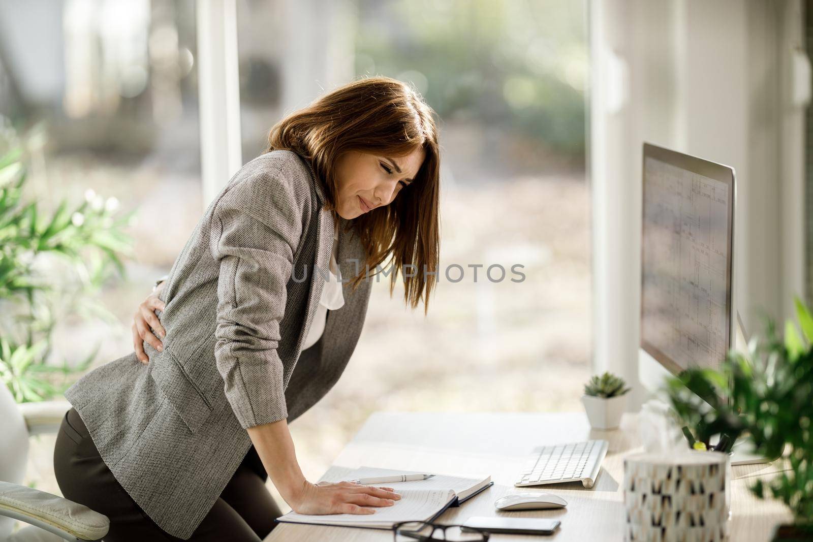 An attractive business woman experiencing back pain while working on computer in a modern office.