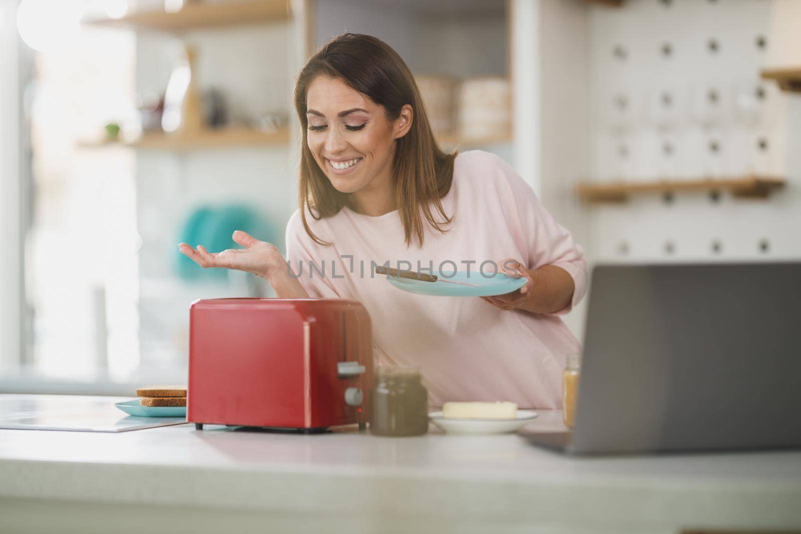 Shot of a young woman roasting a piece of toast in toaster for breakfast at home.