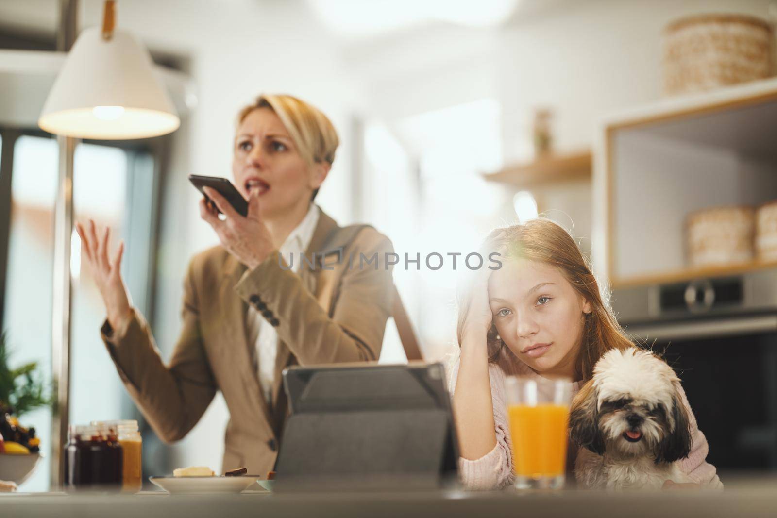 Shot of a frustrated teenage girl sitting with her cute dog waiting for her stressed mom to finish talking on smart phone at her home while getting ready to go to work.