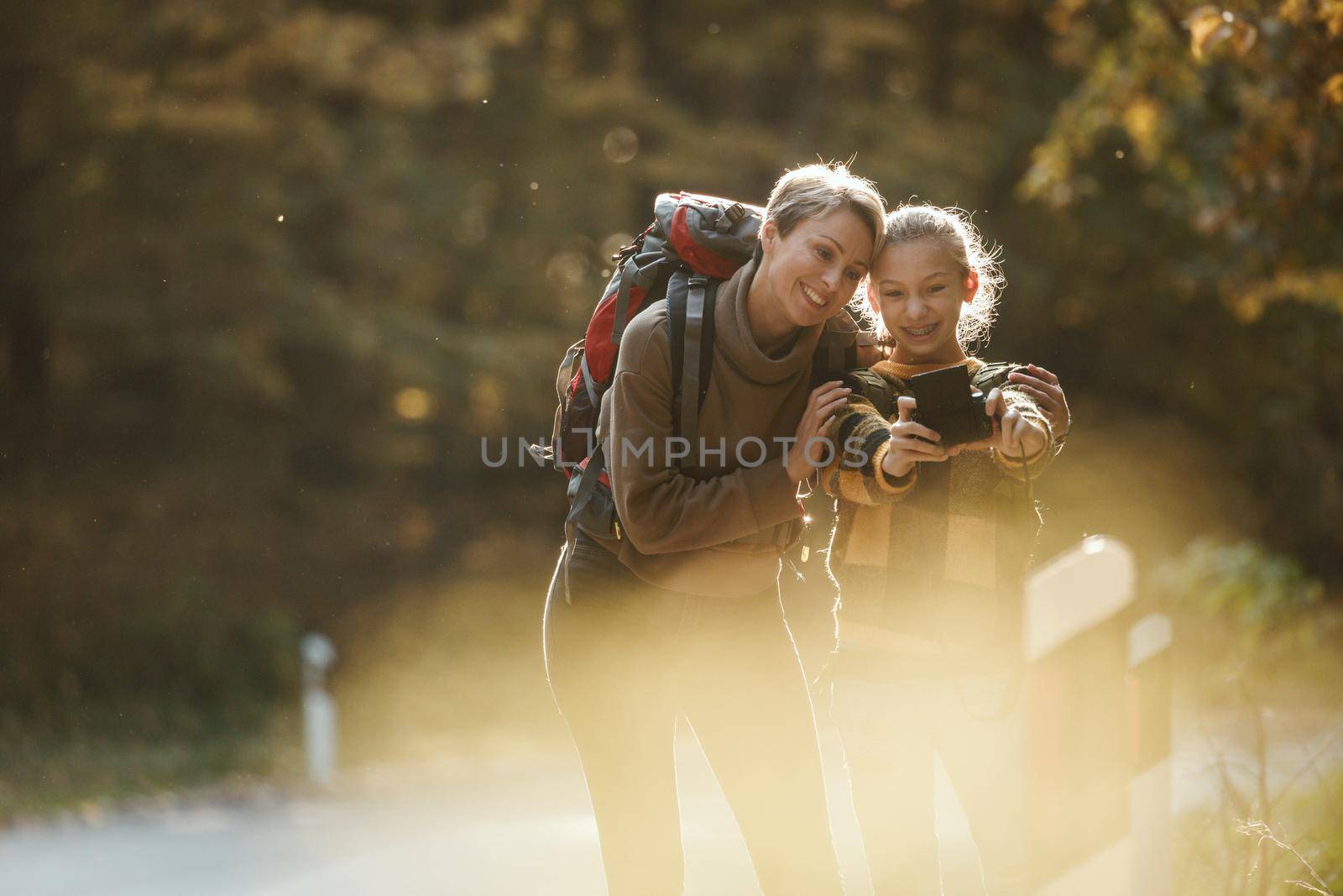 Shot of a teen girl and her mom taking a selfie with digital photo camera during walk together through the forest in autumn.