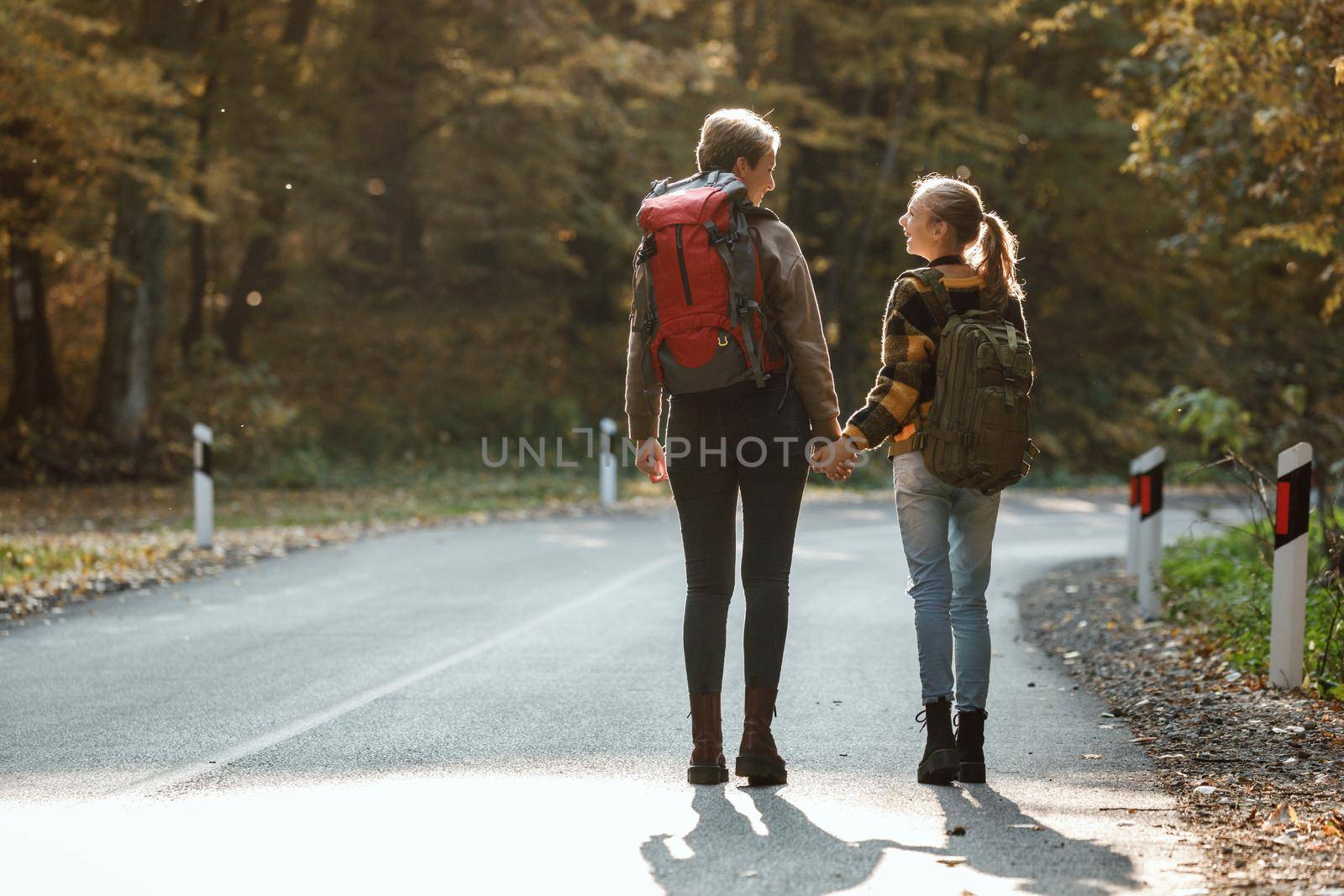 Rearview shot of a teen girl and her mom walking together through the forest in autumn.