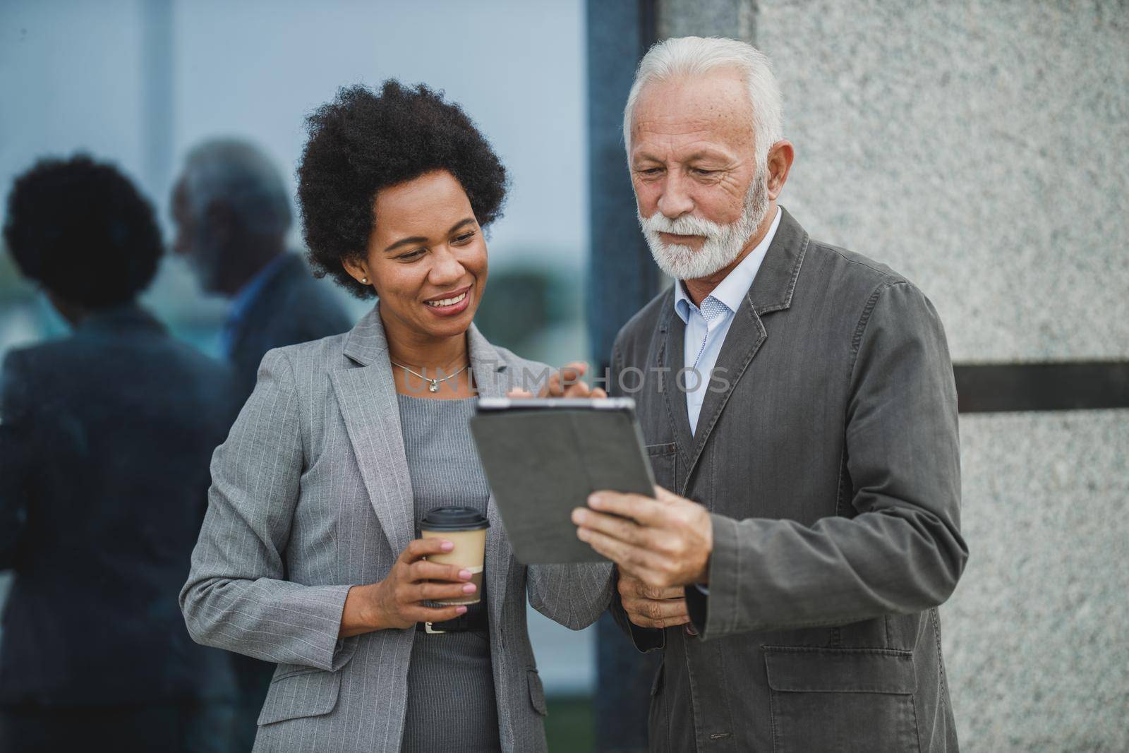 Shot of two successful multi-ethnic business people using digital tablet and having a discussion during a coffee break in front of the office building.