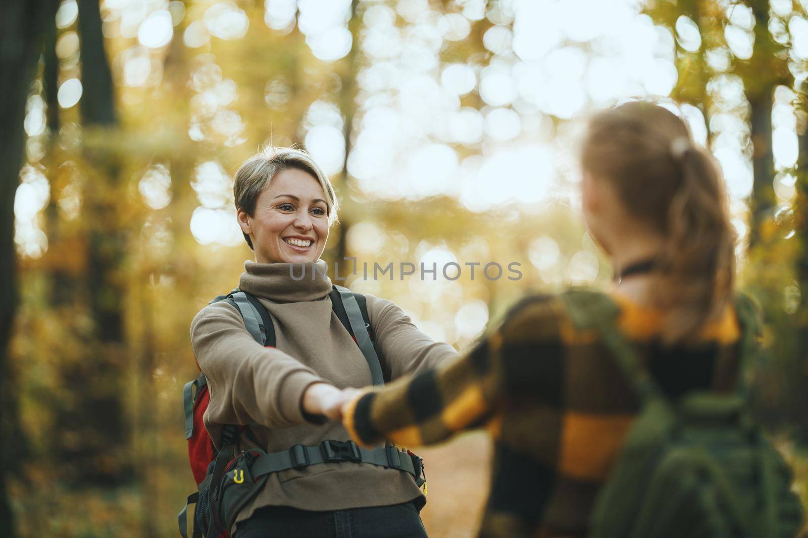 Shot of a teen girl and her mom having fund during walk together through the forest in autumn.