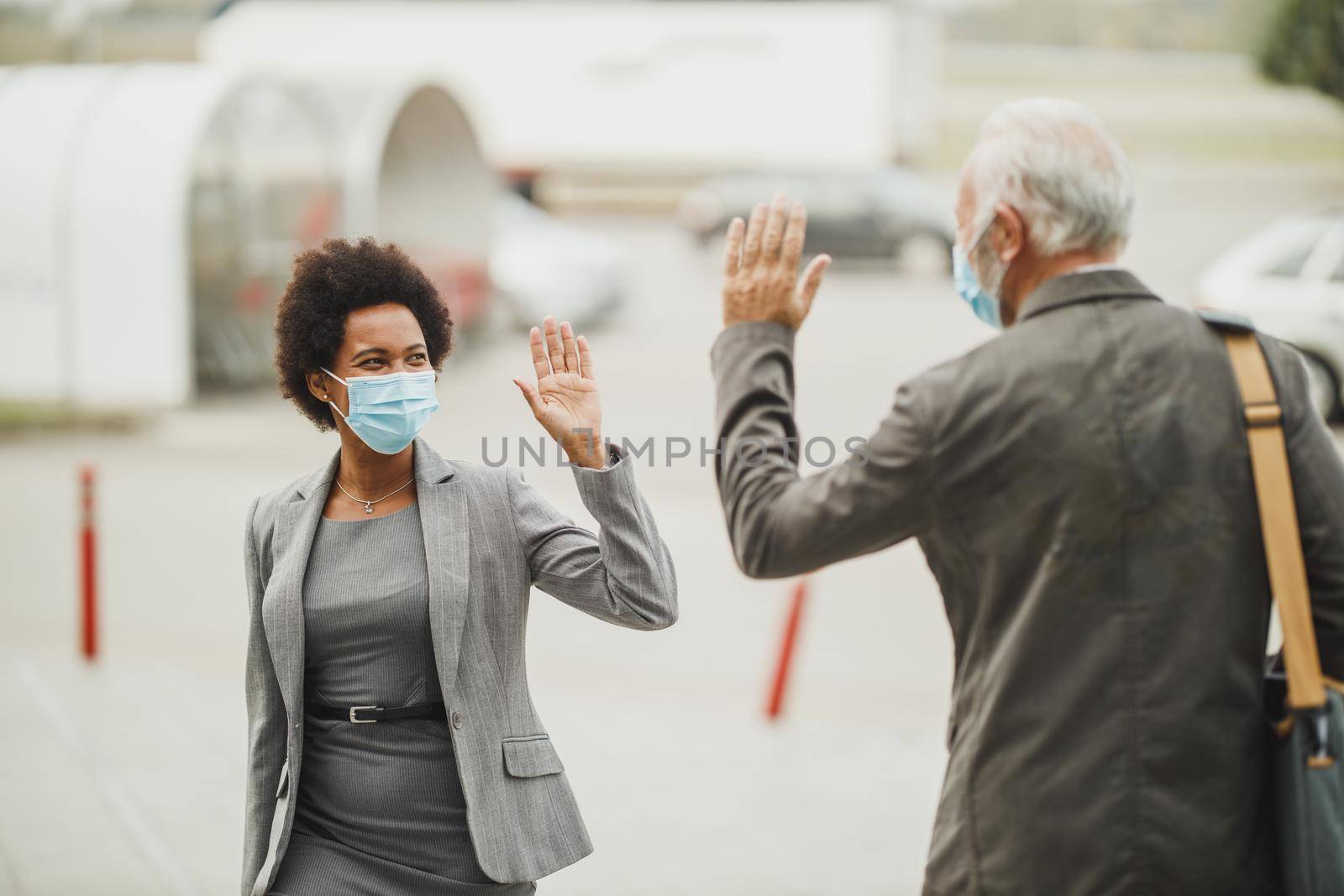 Shot of successful black businesswoman and her senior male colleague using protective mask and greeting with wave hands during COVID-19 pandemic to avoid handshakes.