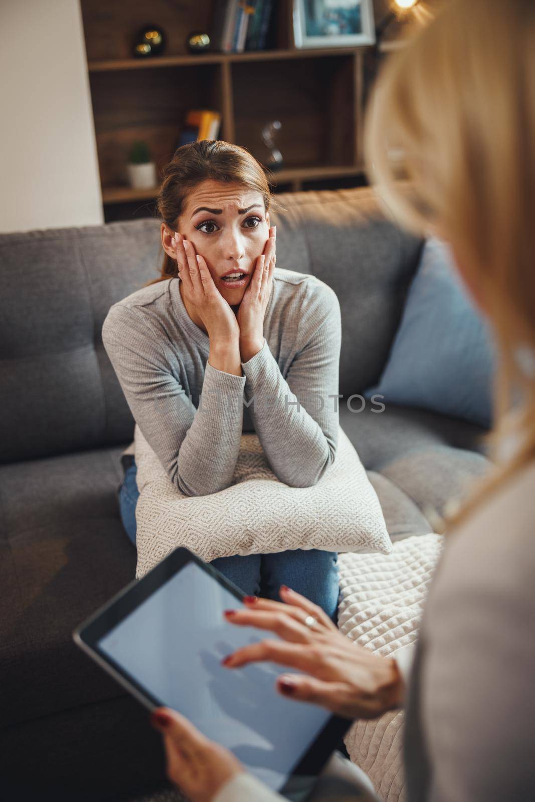 Shot of a stressed out young woman having a discussion with her female psychotherapist while being seated on a sofa inside of a living room.