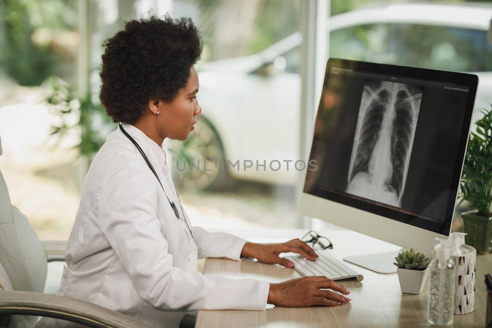 Shot of an African female doctor sitting alone in her consulting room and looking X-ray on computer during COVID-19 pandemic.