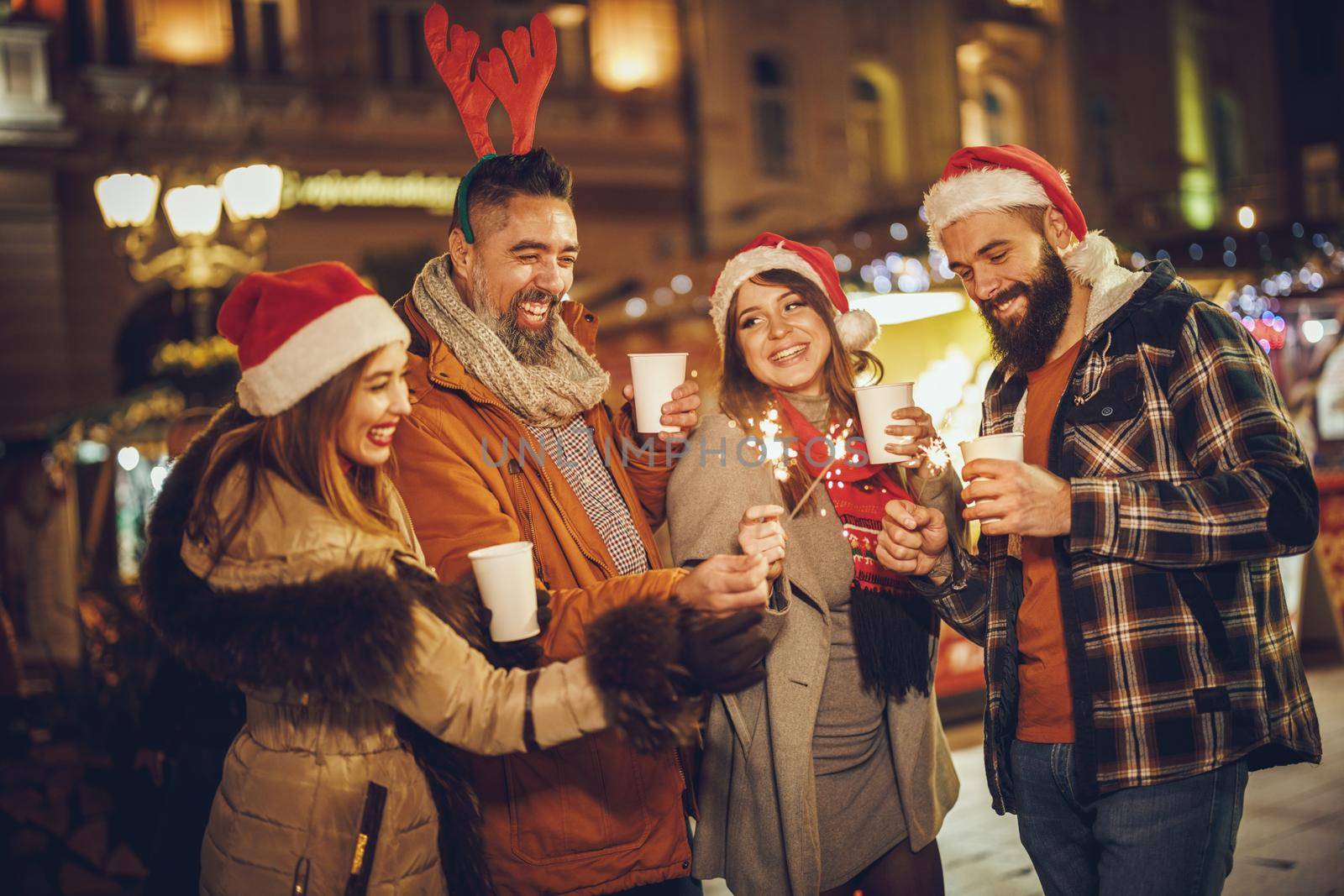 Shot of a group of cheerful young friends having fun with sparklers  and enjoying hot drink on the Christmas market at an evening party.