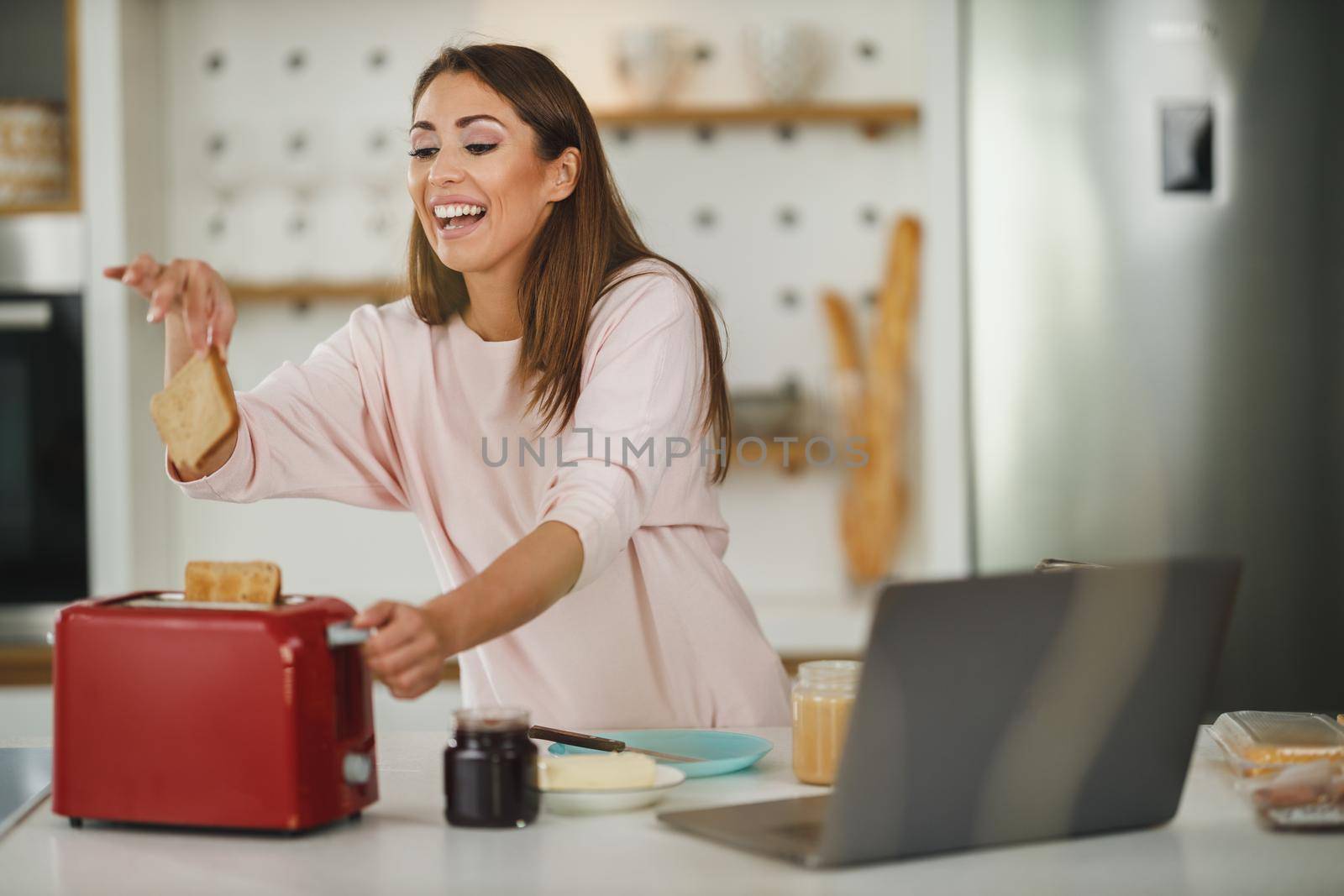 Shot of a young woman roasting a piece of toast in toaster for breakfast at home.