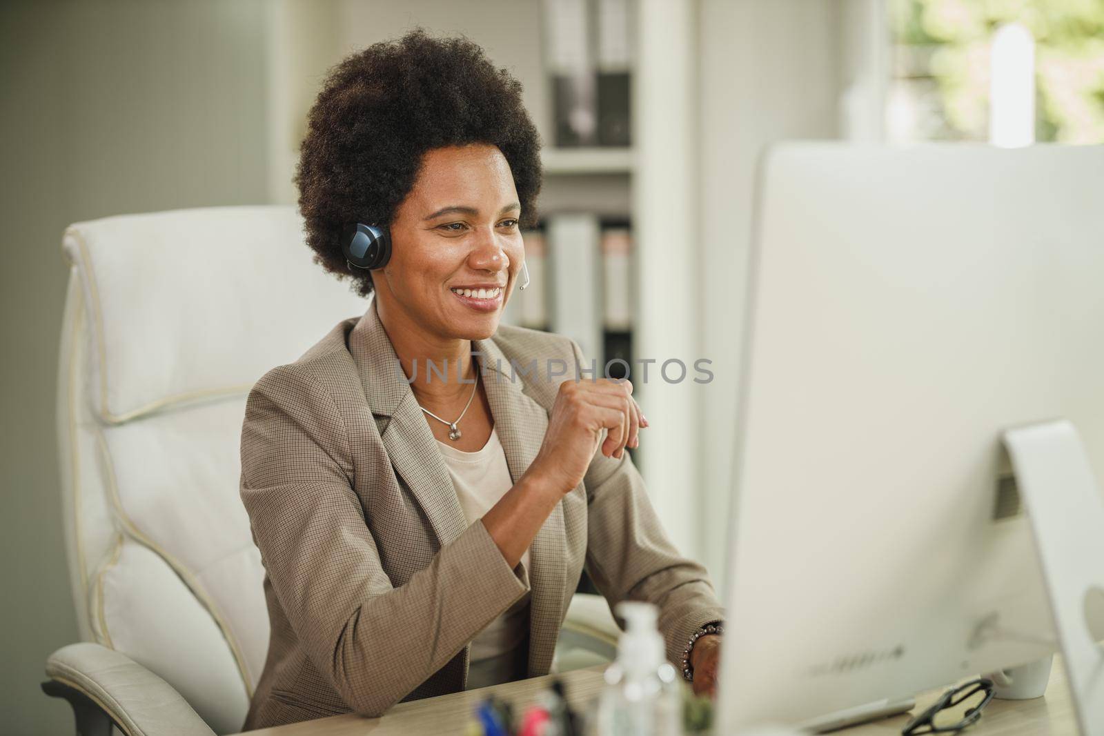 Shot of an attractive African businesswoman sitting alone in her office with headphones and working on computer during corona virus pandemic.