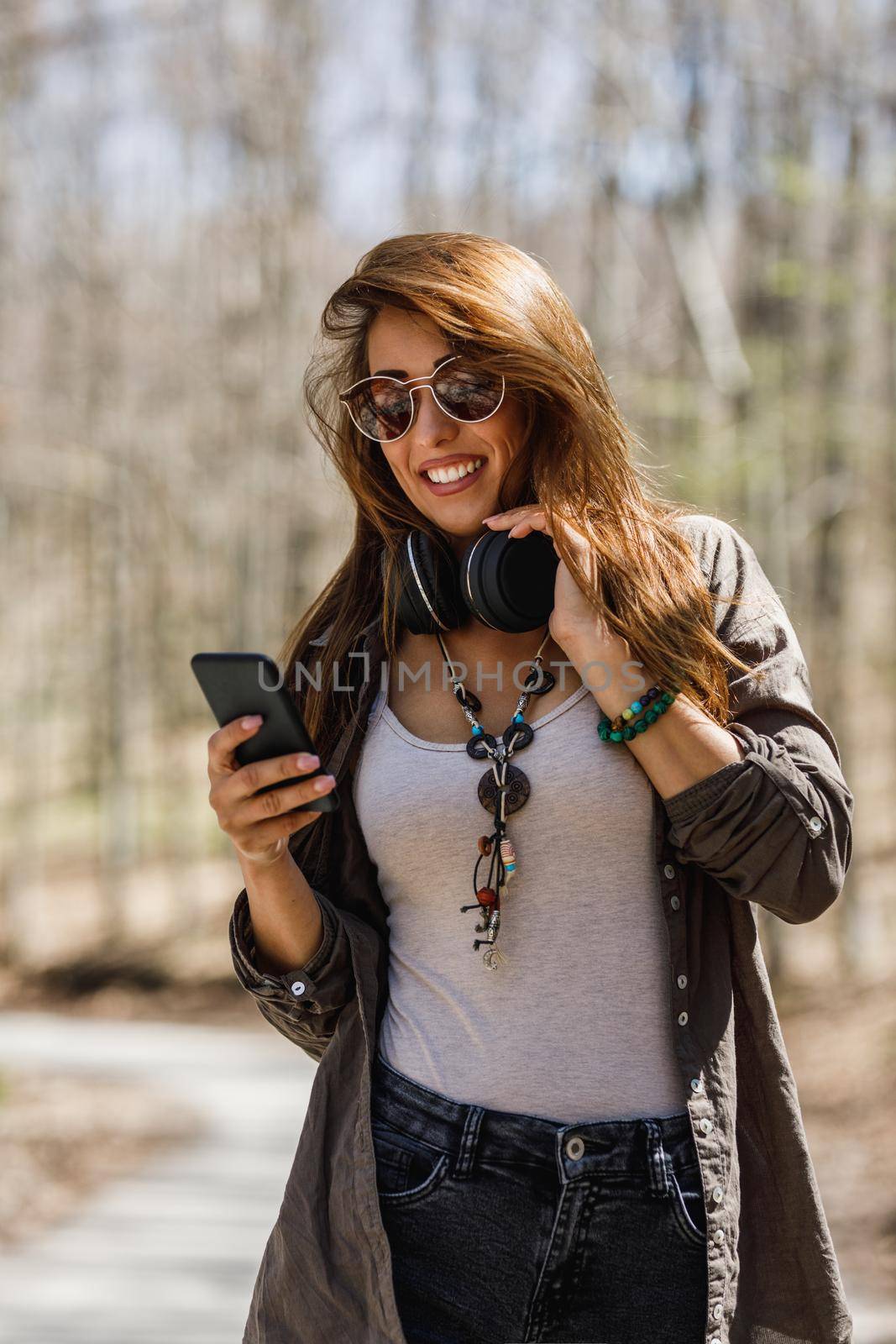 Shot of a smiling young woman using her smartphone while walking in nature.
