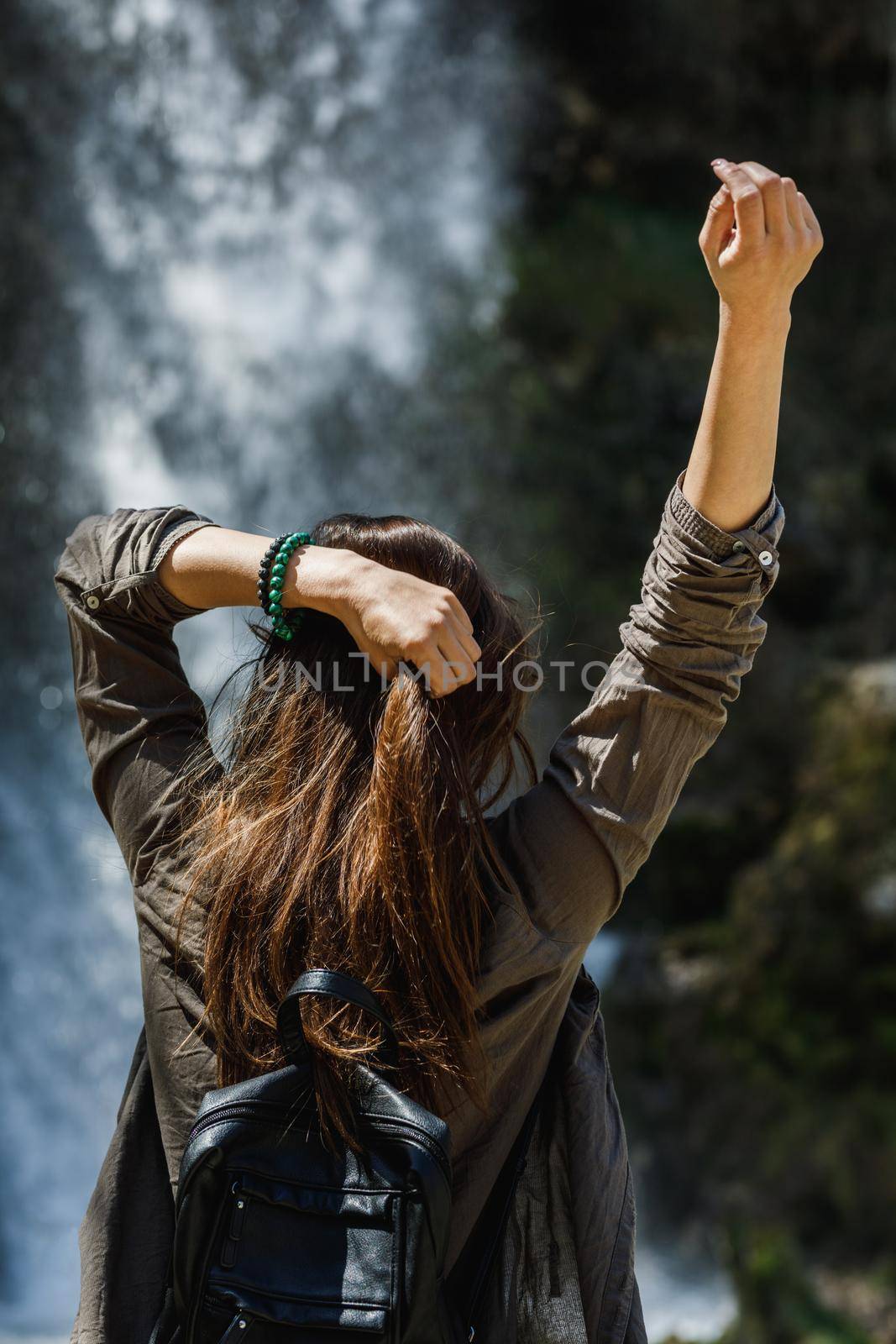 Rear view of a happy woman enjoying the view of the beautiful waterfall.