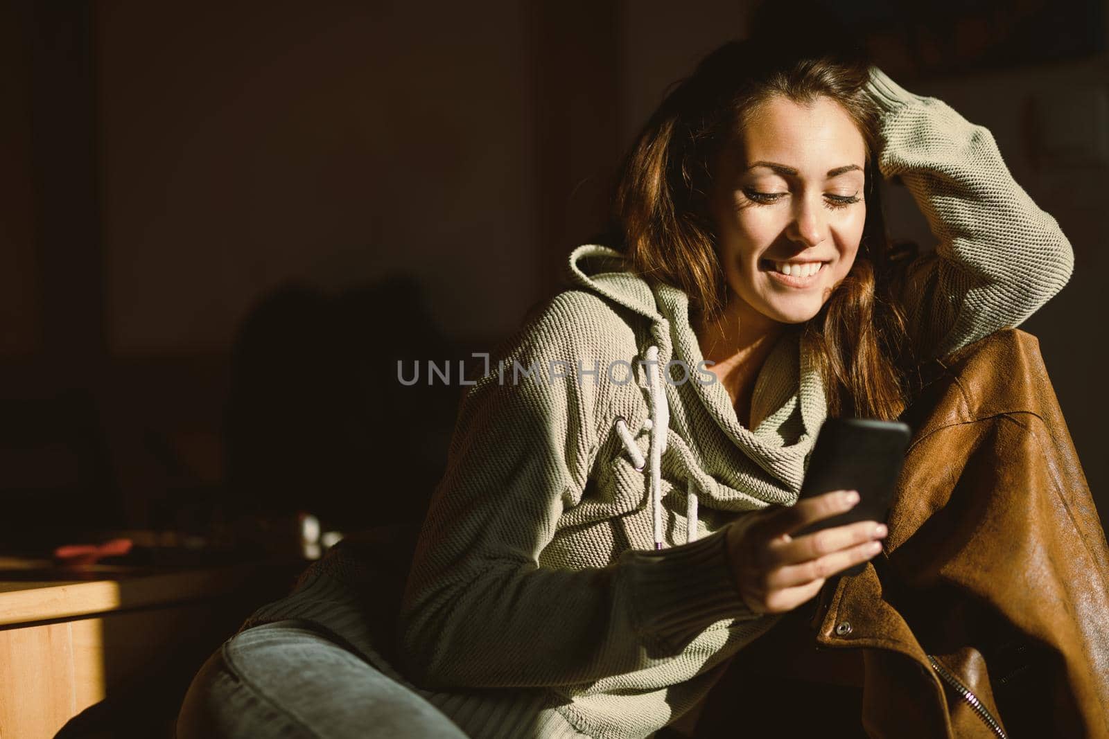 A young happy woman using her smartphone, relaxing and enjoying a sunny morning in the room.