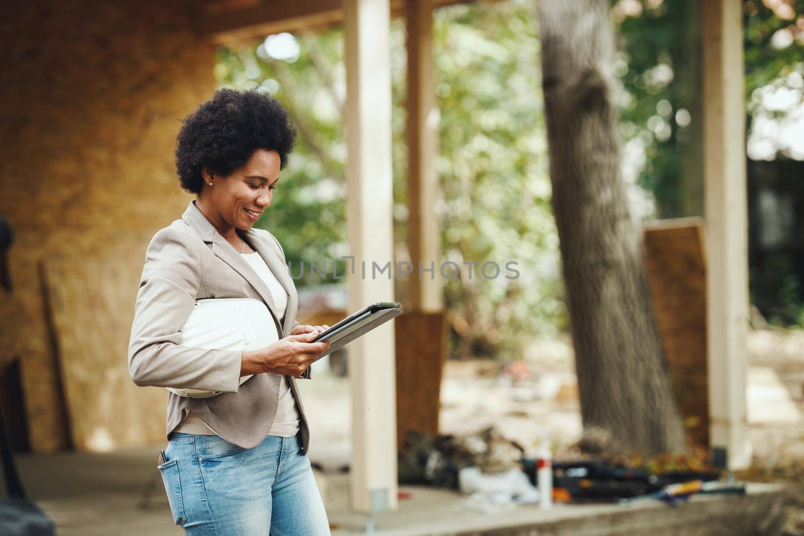 Shot of an African female architect using a digital tablet and checking construction site of a new wooden house.