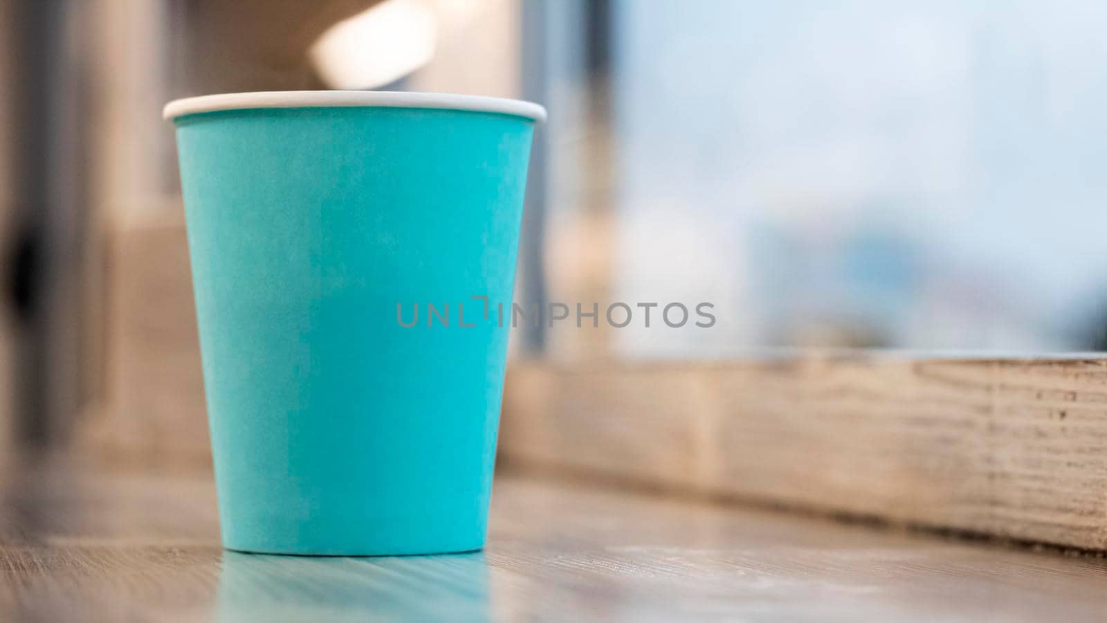 Blue paper cup with coffee on a wooden table, copy space