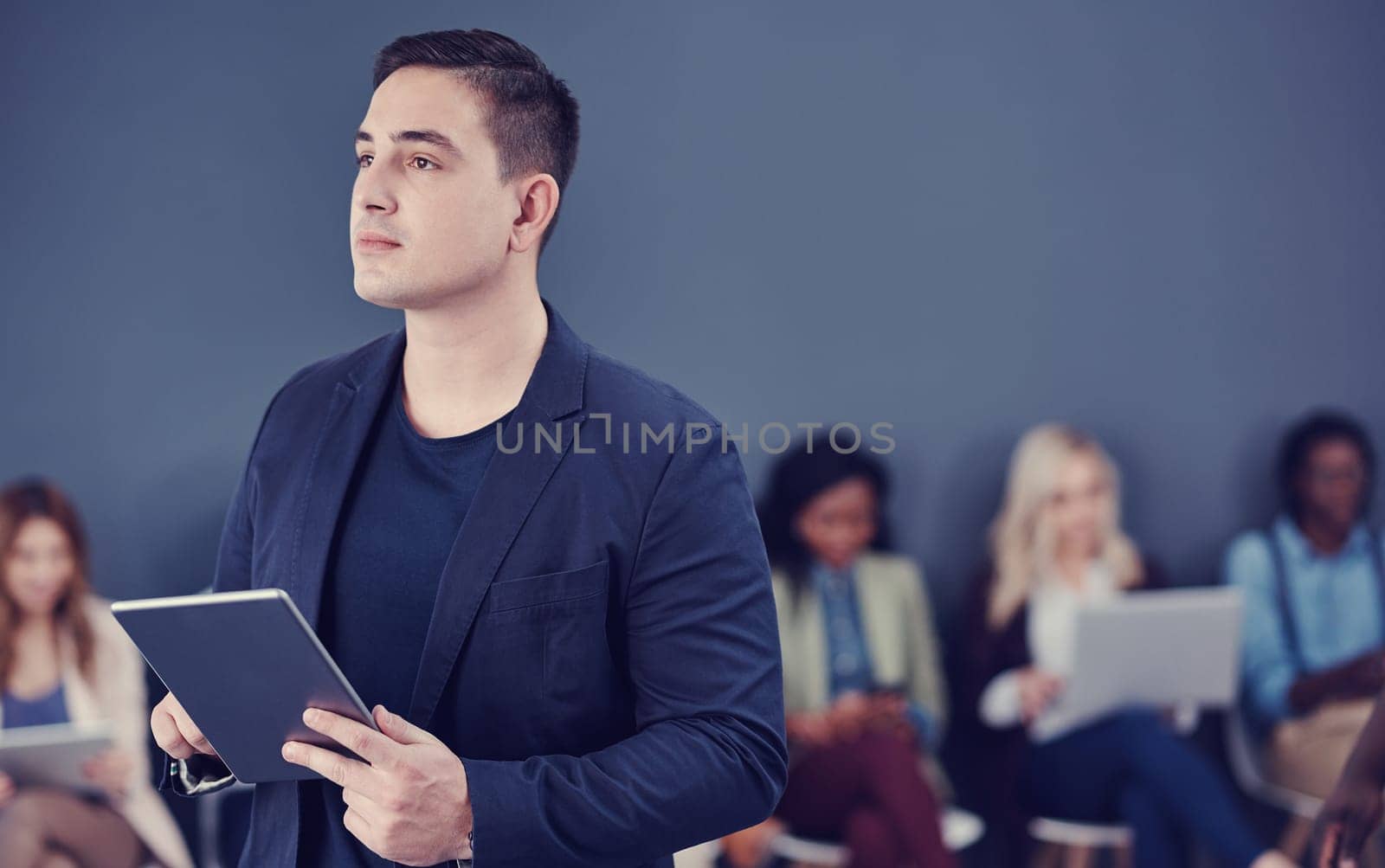 He does everything with the future in mind. a handsome young businessman using a tablet with his colleagues in the background