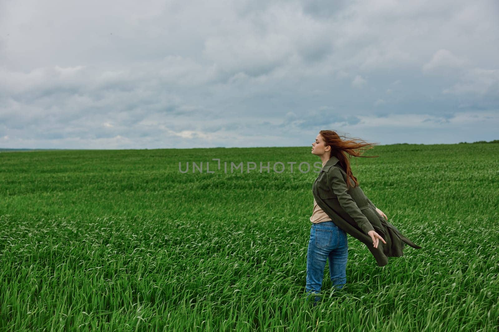 a woman in a long coat stands in tall green grass in a field, in cloudy weather, enjoying nature and the view. High quality photo