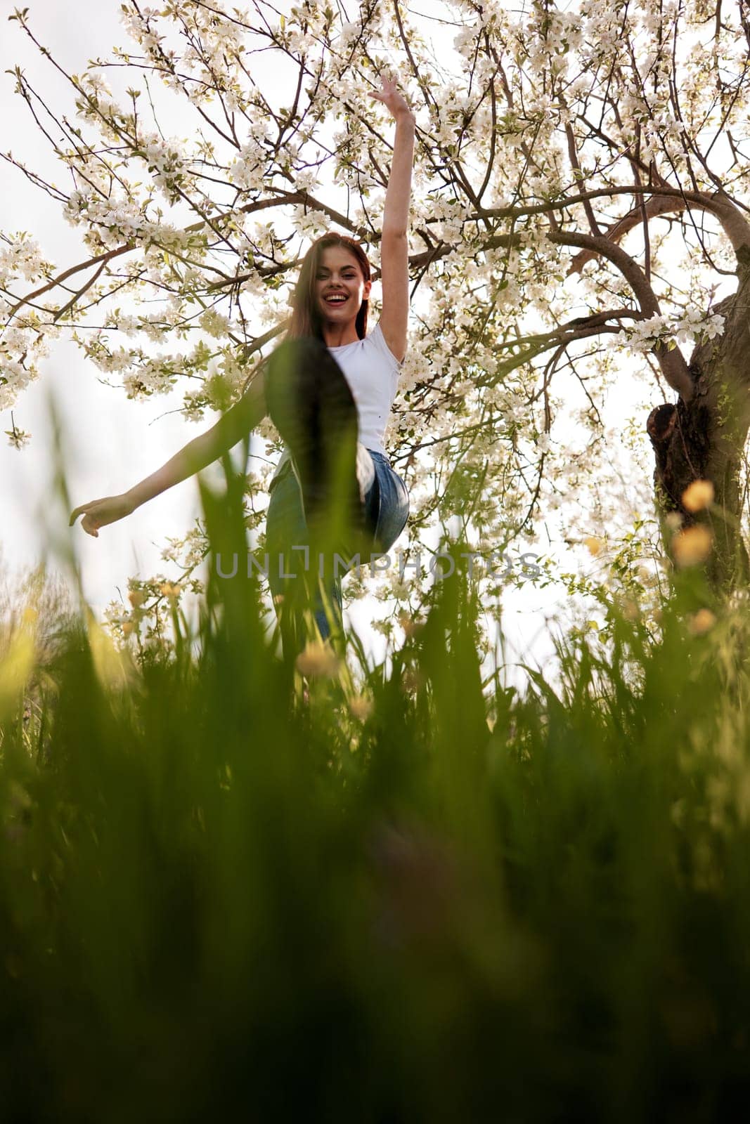 active woman posing raising her leg up against the background of a flowering tree in the park by Vichizh