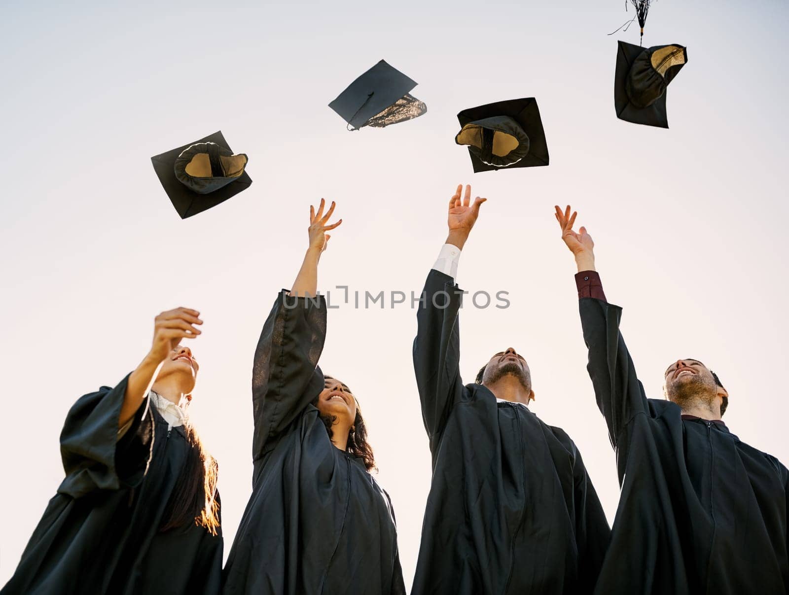 Even if its tough, you can still triumph. a group of students throwing their hats in the air on graduation day. by YuriArcurs