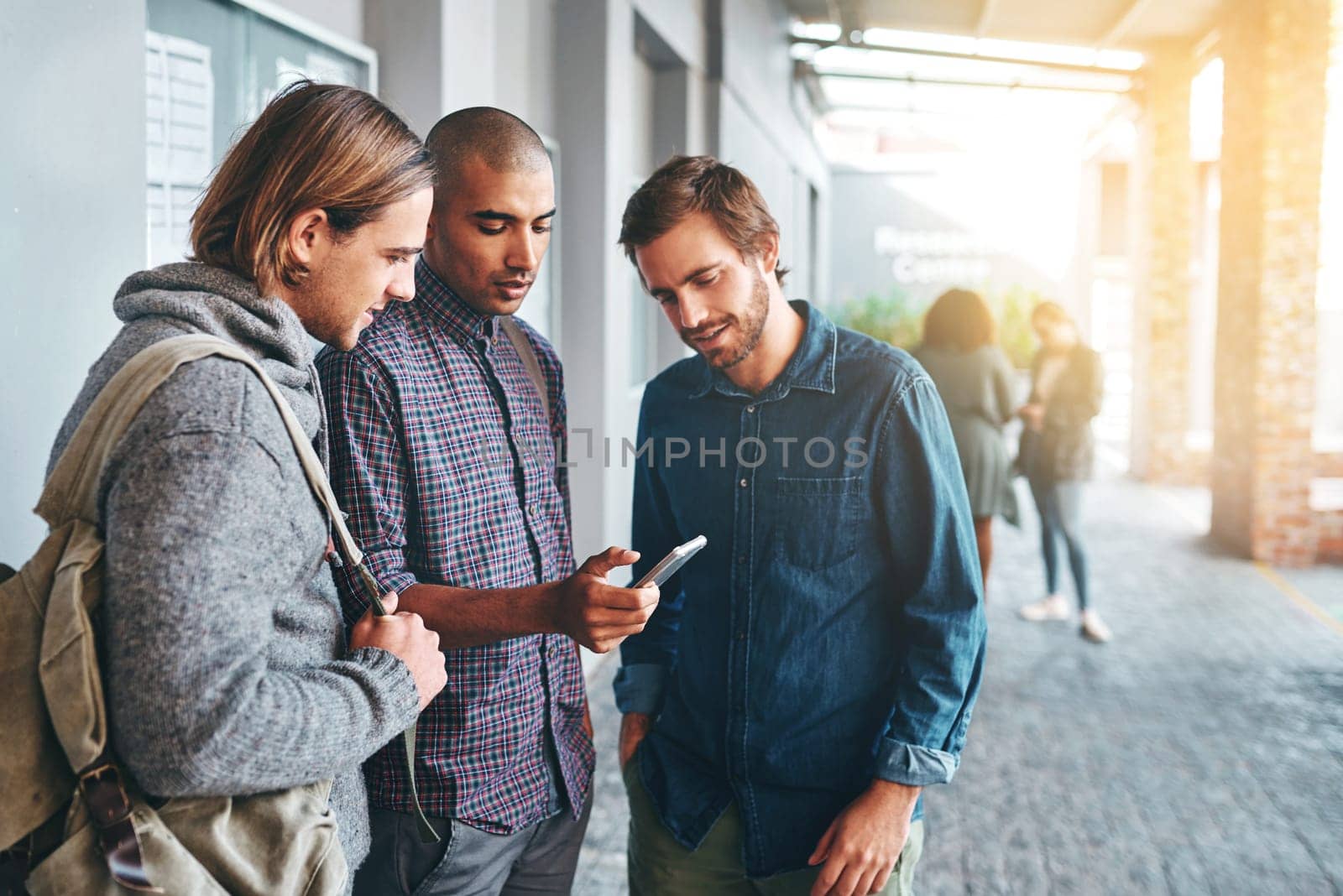 Im sending the exam timetable to you guys. a group of young students using a smartphone together outdoors on campus. by YuriArcurs