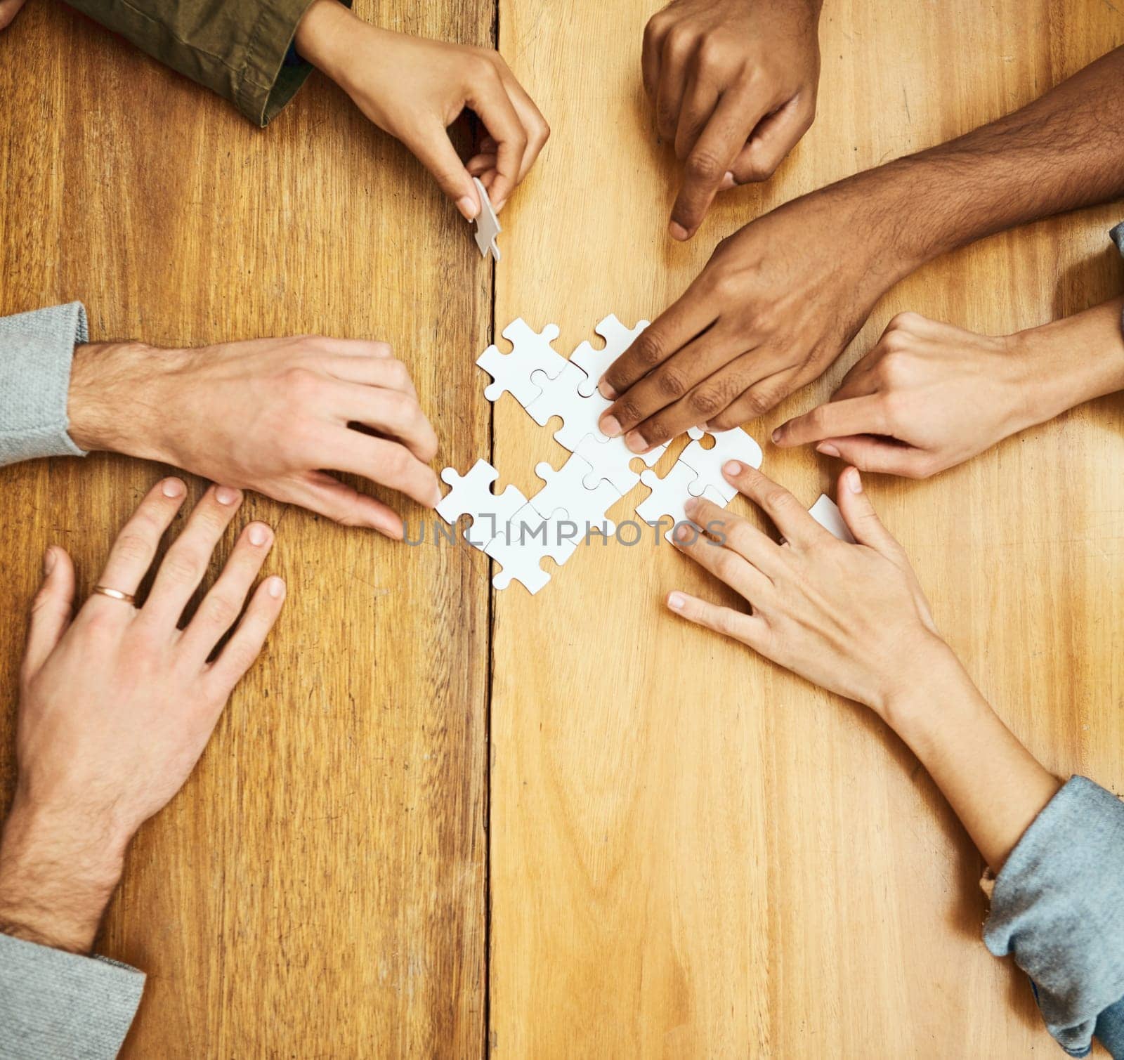 Putting it all together. High angle shot of a group of unrecognizable university students building a puzzle while studying in the library. by YuriArcurs