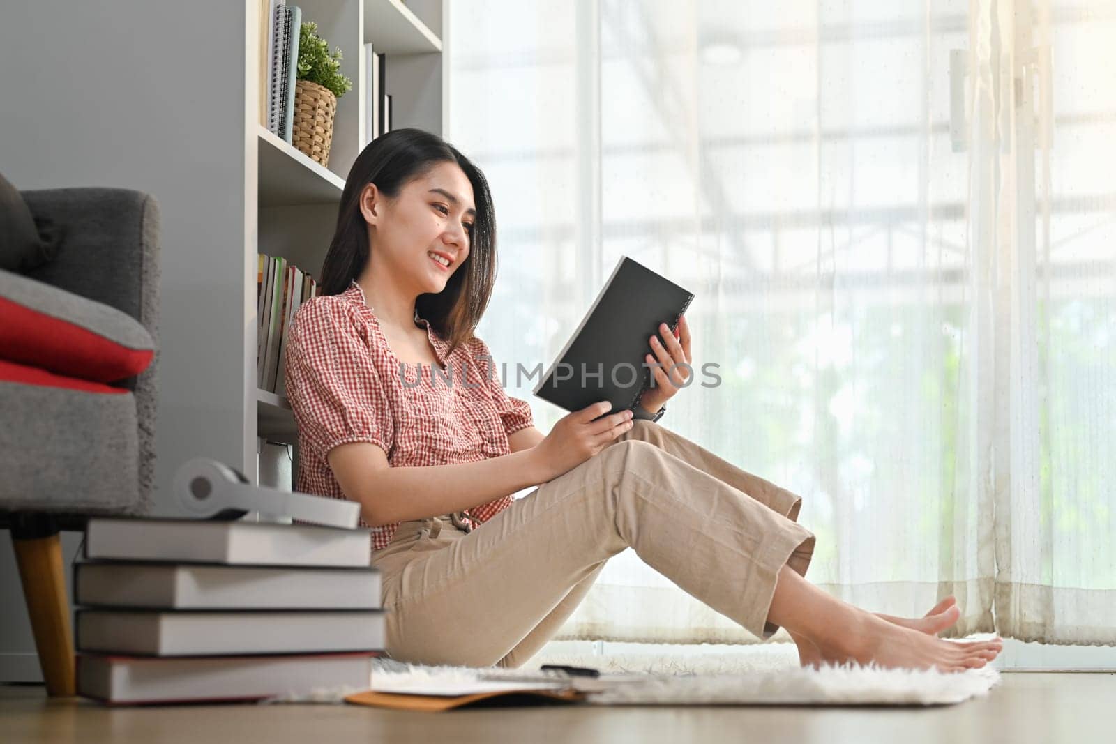 Bottom view of beautiful woman sitting floor in living room and reading a book, spending leisure weekend time at home.