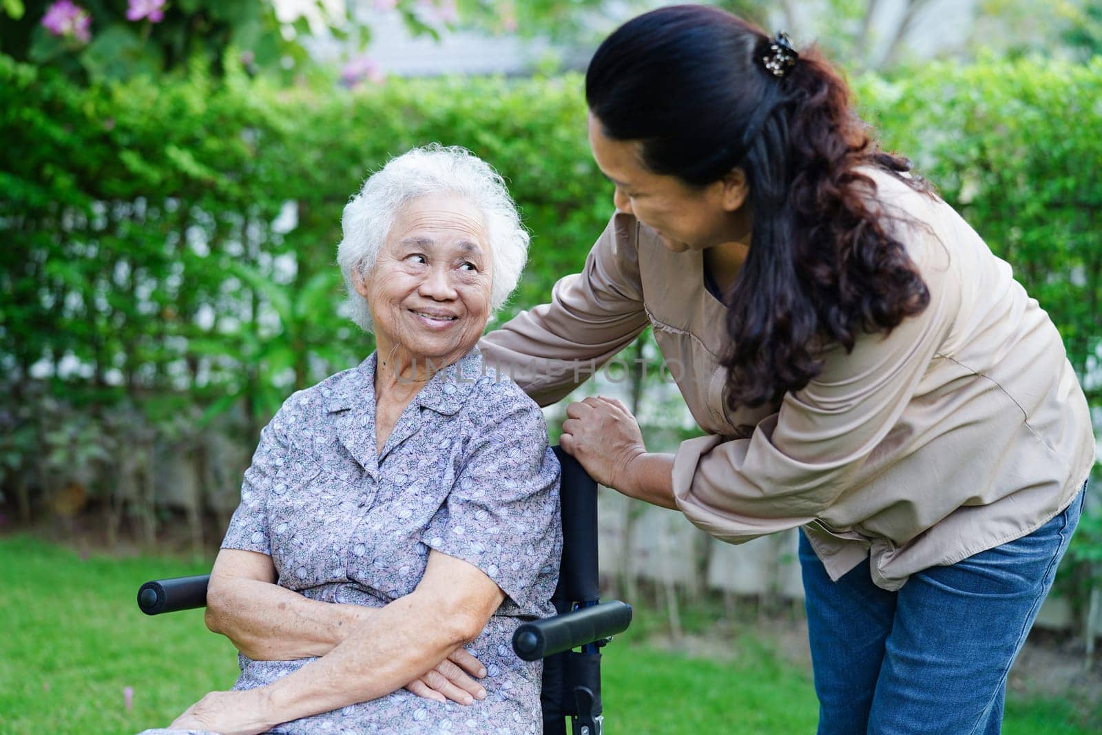 Caregiver help Asian elderly woman disability patient sitting on wheelchair in park, medical concept.