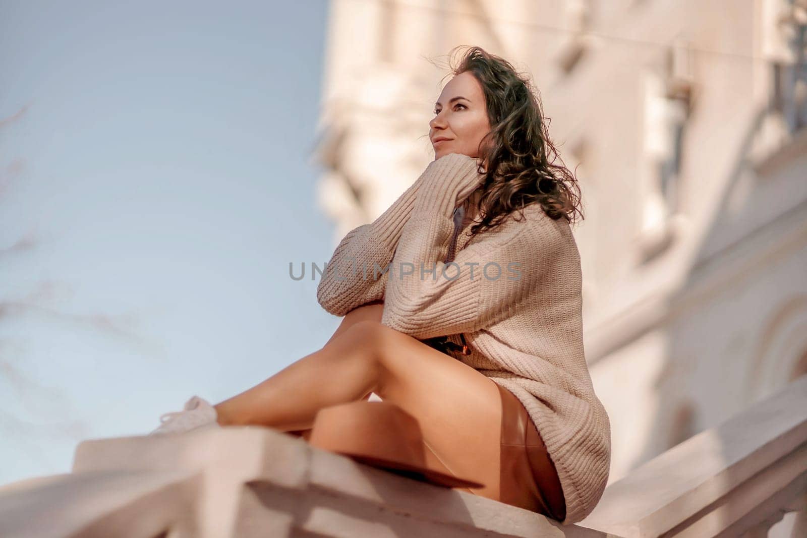 Portrait of a woman in front of a building and blue sky. Dressed in a loose light sweater, brown skirt. Tourism, walking around the sights of the city