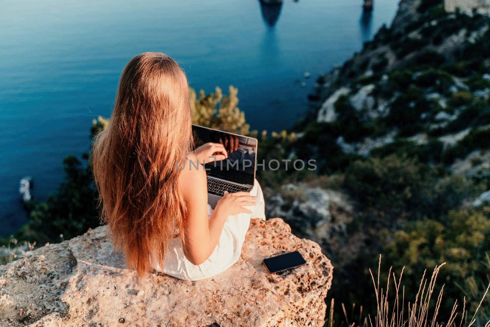 Freelance women sea working on the computer. Good looking middle aged woman typing on a laptop keyboard outdoors with a beautiful sea view. The concept of remote work. by Matiunina