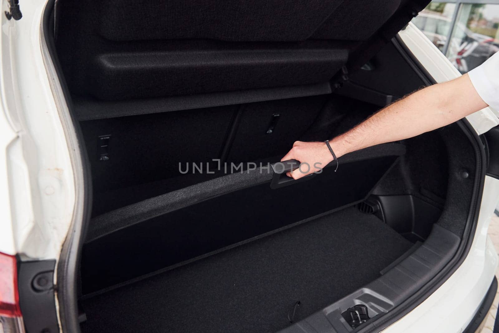 Woman's hands opening car trunk. Close up view. White modern automobile.
