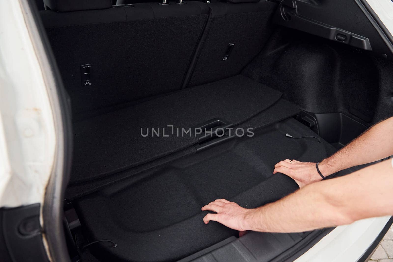 Woman's hands opening car trunk. Close up view. White modern automobile.