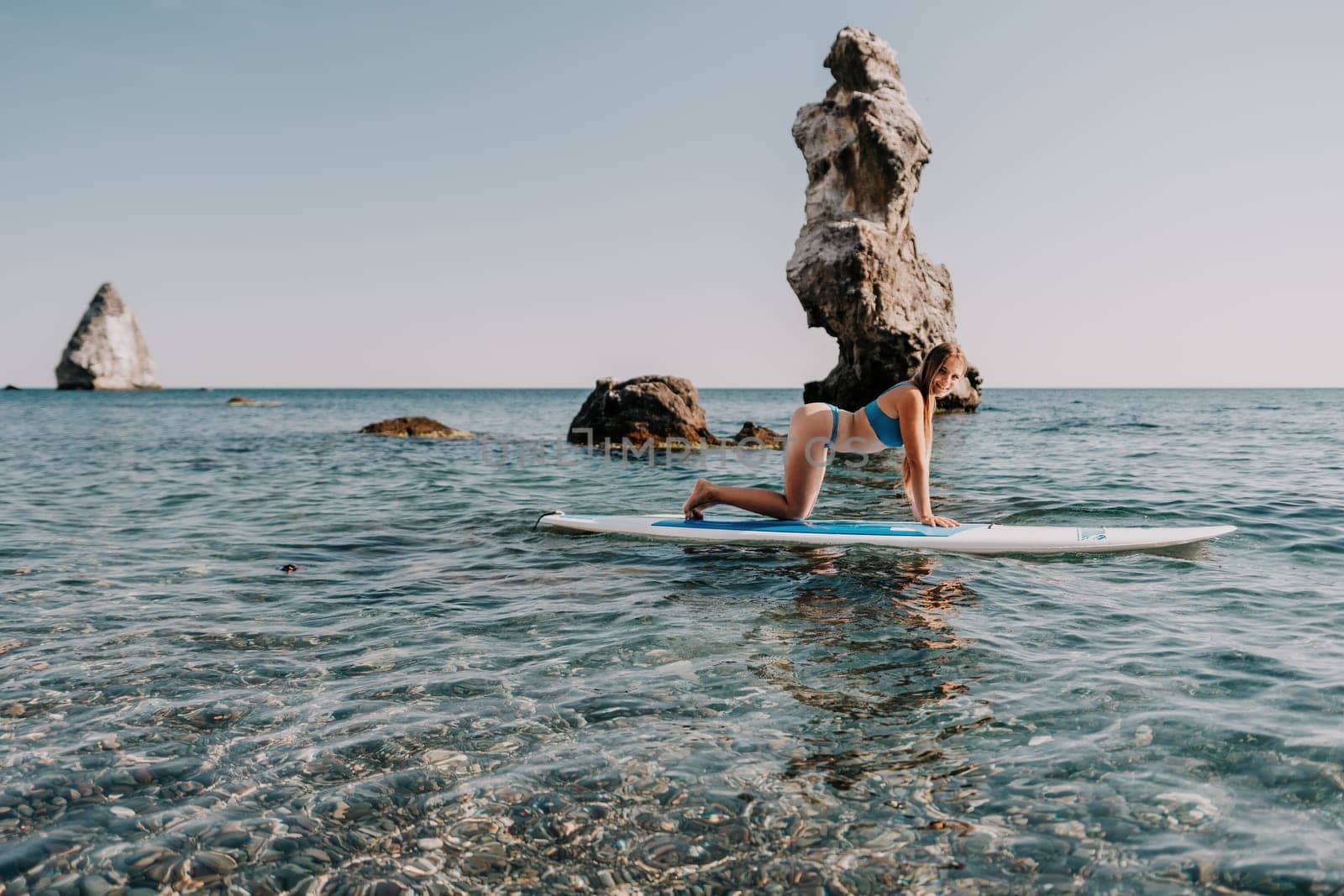 Close up shot of happy young caucasian woman looking at camera and smiling. Cute woman portrait in bikini posing on a volcanic rock high above the sea