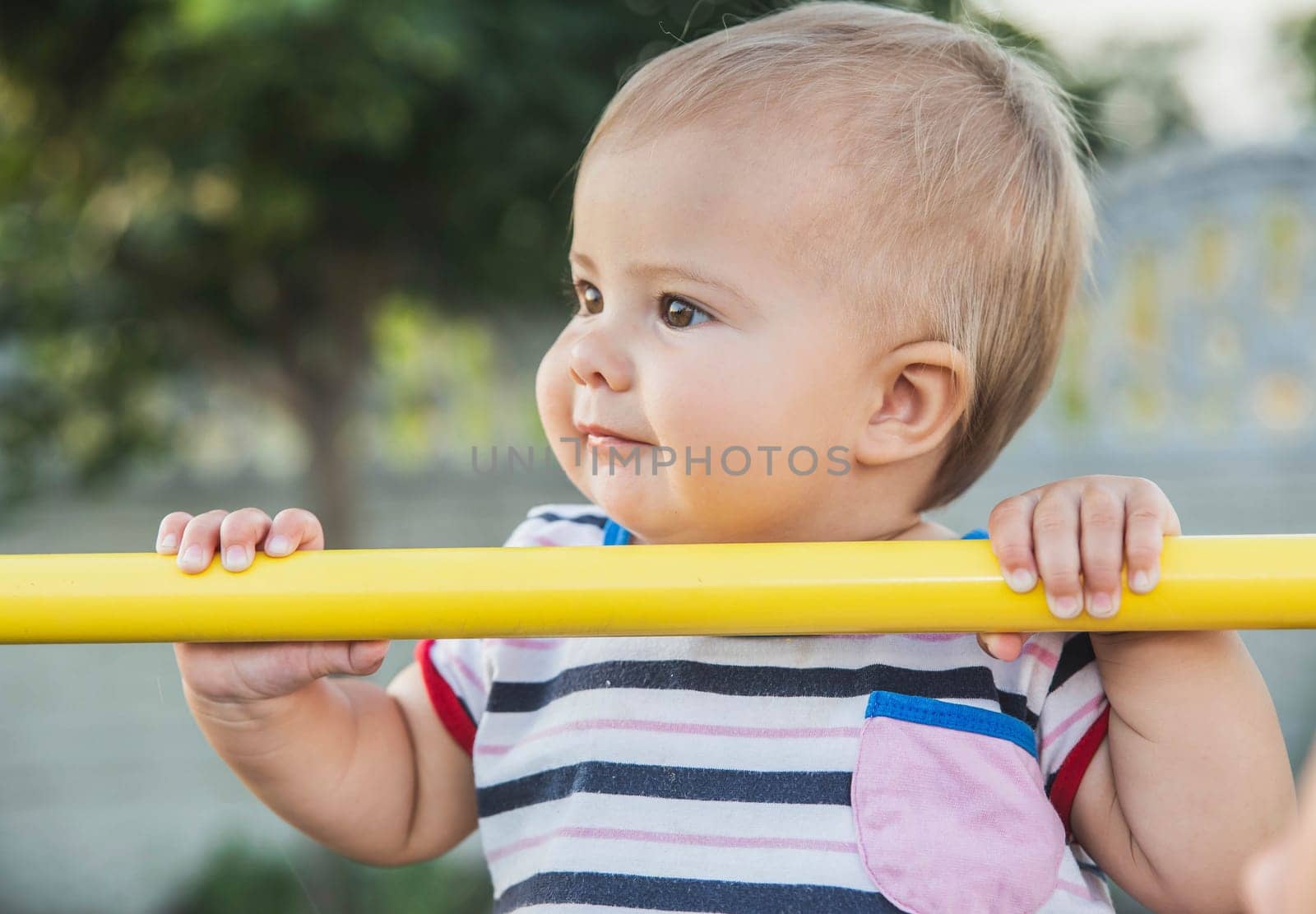 beautiful blonde baby pulls herself up on the horizontal bar.