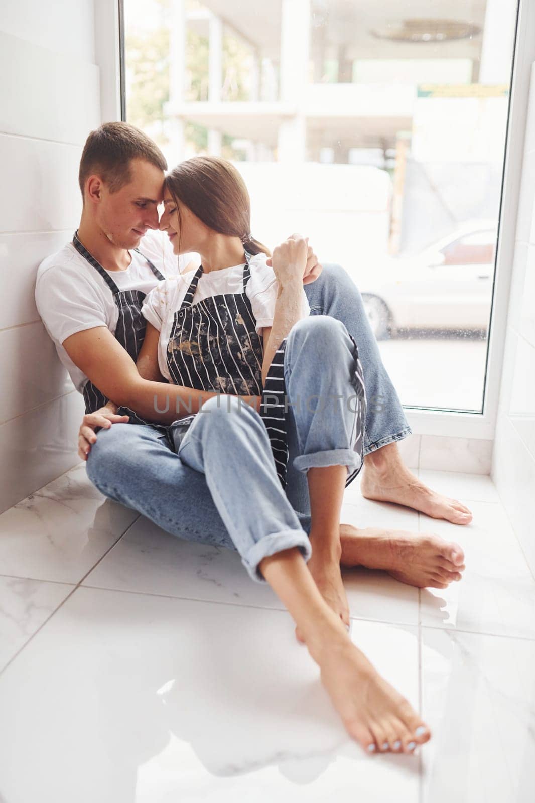 Cute young couple in jeans sitting down on the floor and embracing each other.