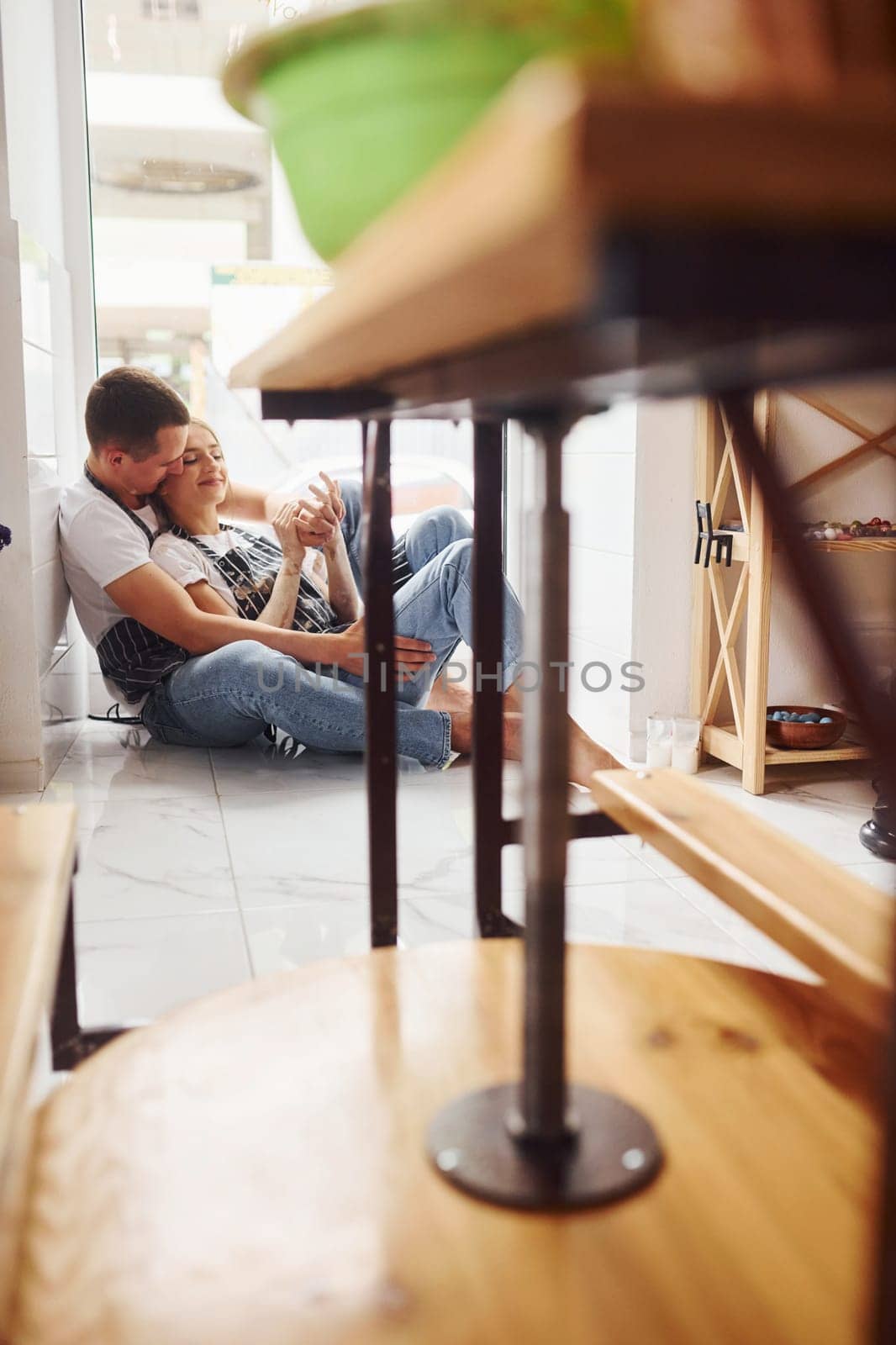Taking a break and sitting on the floor. With her boyfriend or husband. Young female ceramist indoors with handmade clay product. Conception of pottery.