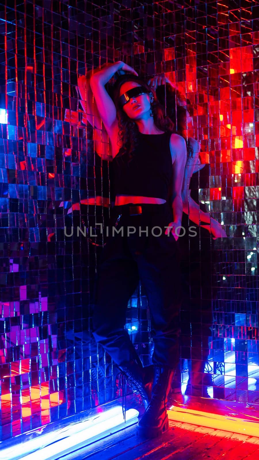 Portrait of a caucasian woman in sunglasses in neon light against a mirror wall