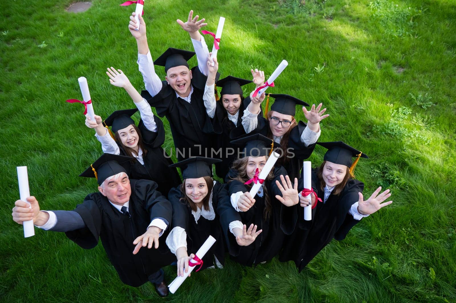 Graduates in robes show off their diplomas outdoors. View from above. Age student