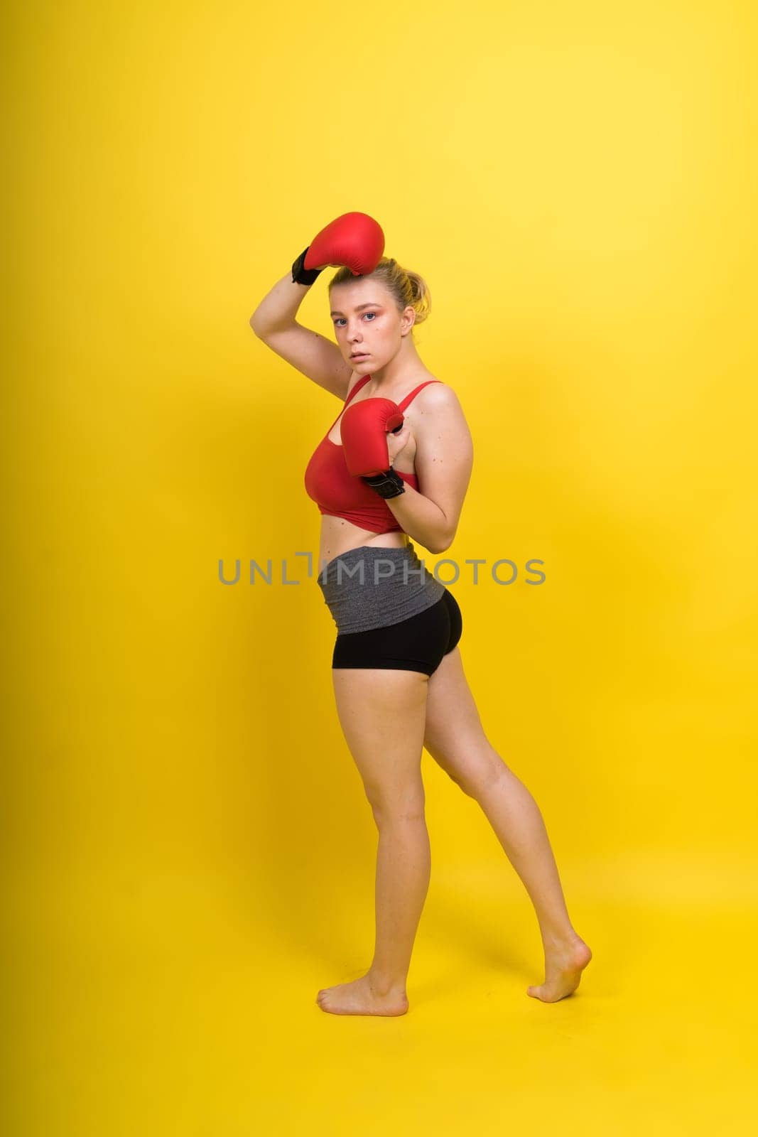 Image of a seductive young woman boxer posing isolated on yellow red background in boxing gloves. by Zelenin