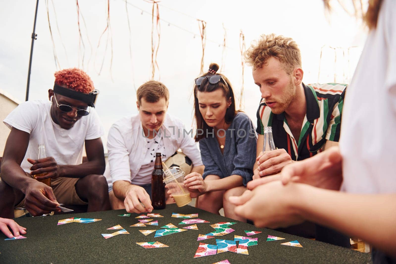 Playing card game. Group of young people in casual clothes have a party at rooftop together at daytime.