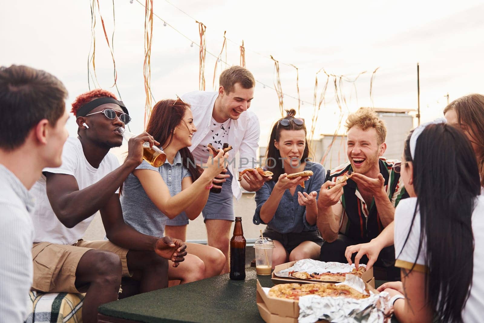 With delicious pizza. Group of young people in casual clothes have a party at rooftop together at daytime.