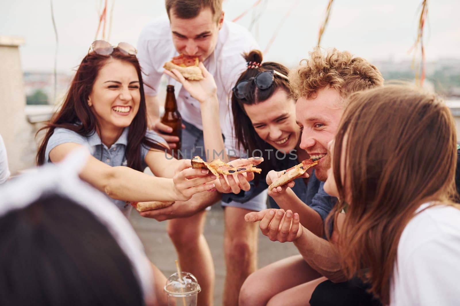 With delicious pizza. Group of young people in casual clothes have a party at rooftop together at daytime.