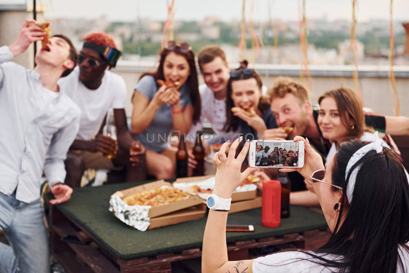 With delicious pizza. Group of young people in casual clothes have a party at rooftop together at daytime.
