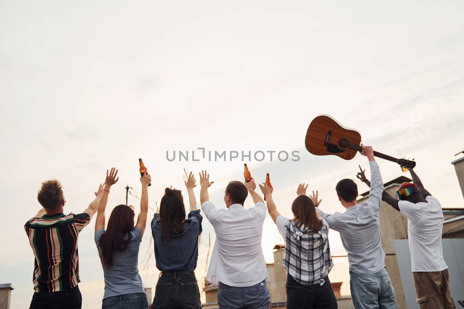 Standing high and looking at the cloudy sky. Group of young people in casual clothes have a party at rooftop together at daytime.