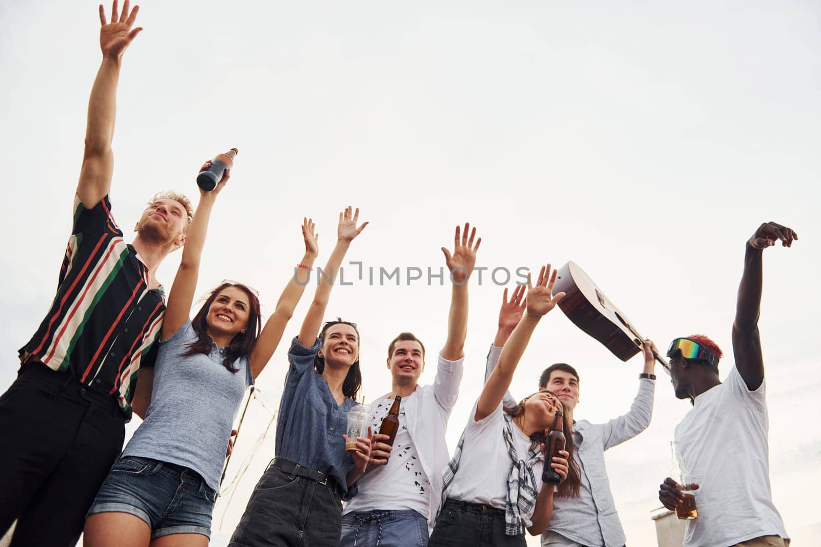 Standing high and looking at the cloudy sky. Group of young people in casual clothes have a party at rooftop together at daytime.