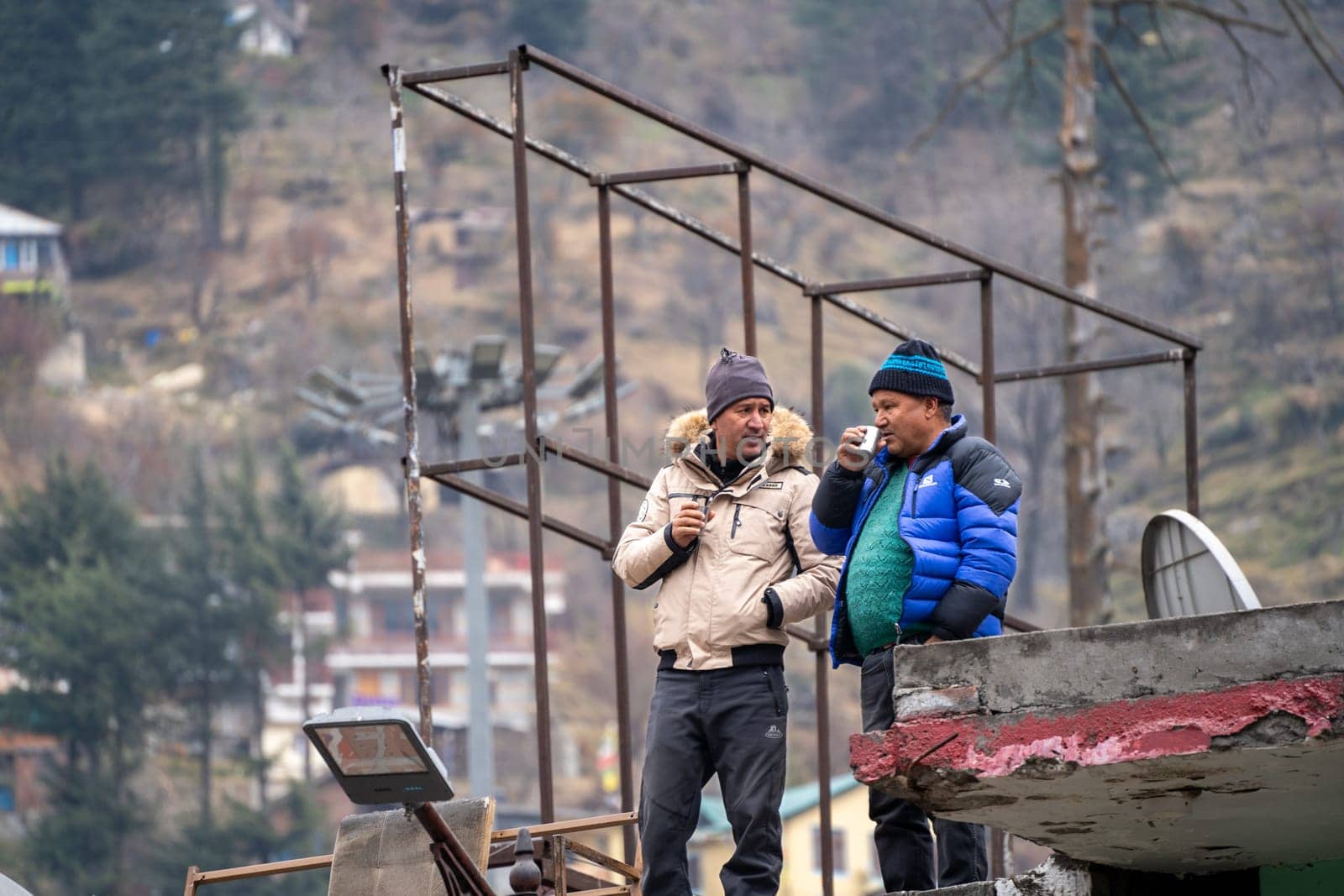 Owners constuction workers sip tea on roof a new shop in manali with mountains in background by Shalinimathur