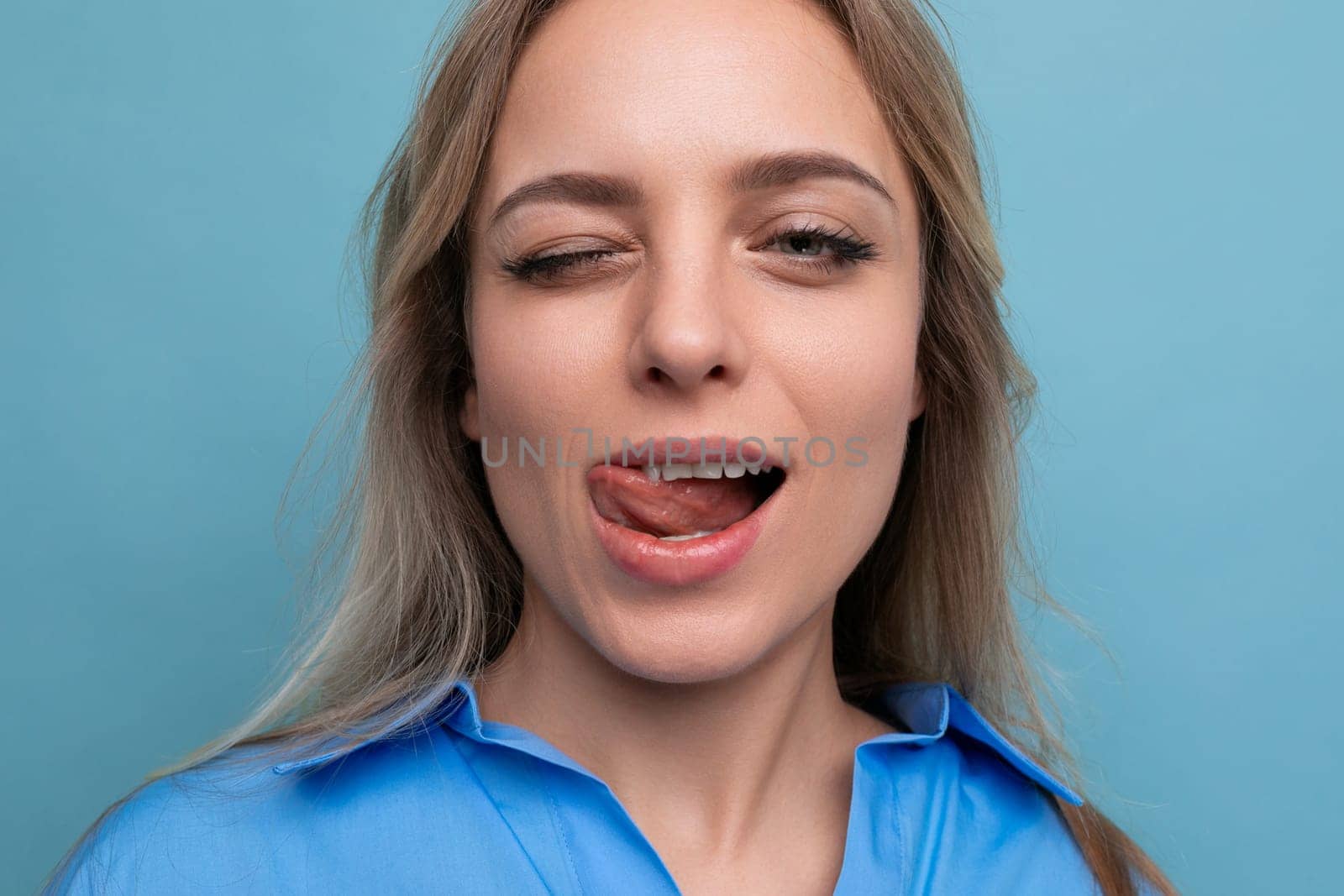 close-up of blond young woman winking on blue background.