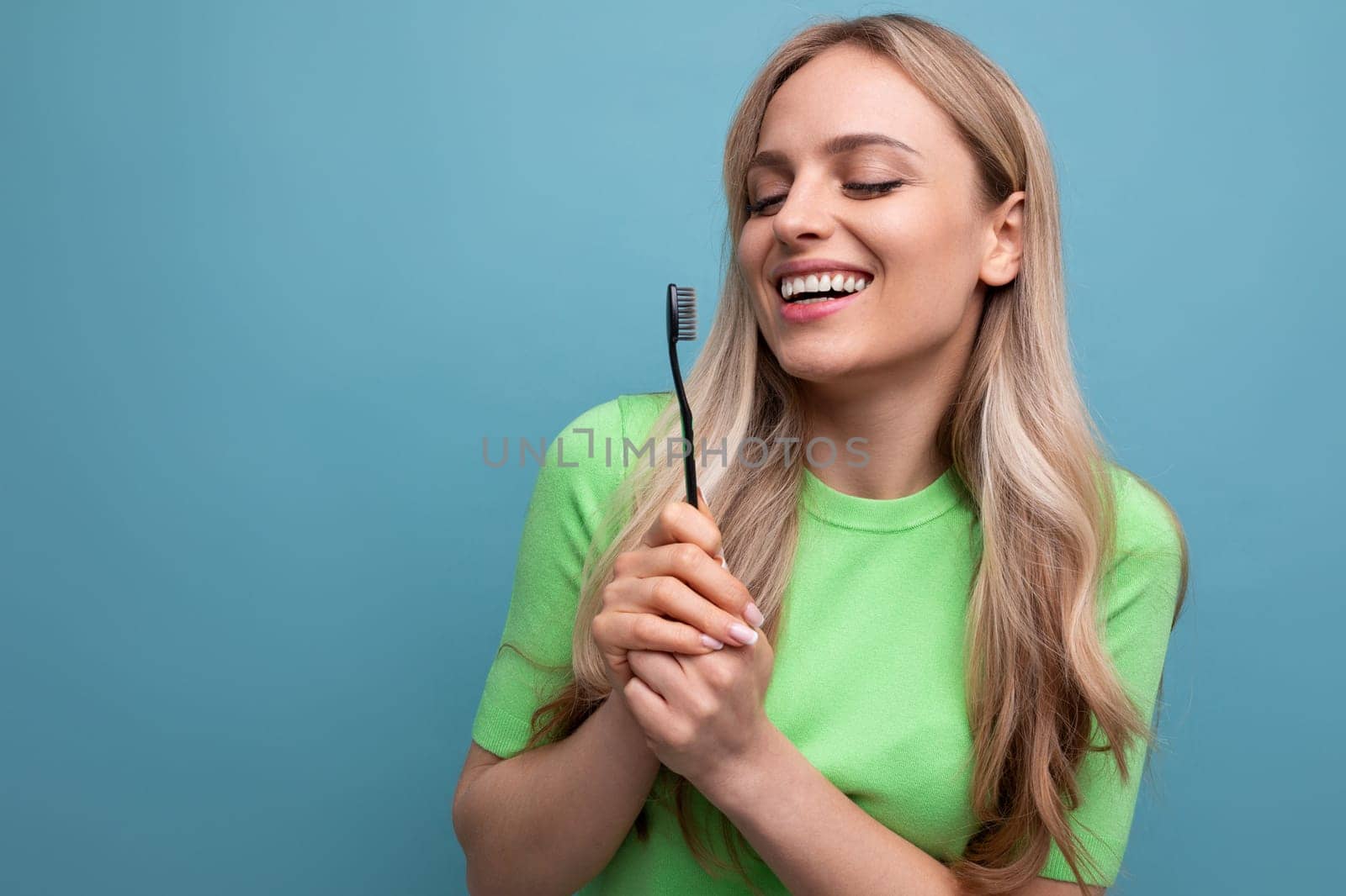 healthy young blond woman with even teeth holding a toothbrush on a blue background by TRMK