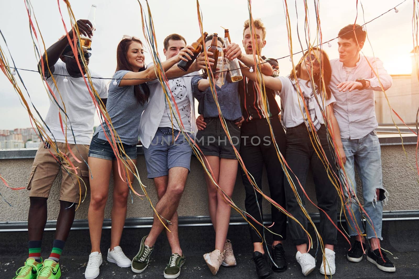 Leaning on the edge of the rooftop with decorates. Group of young people in casual clothes have a party together at daytime.