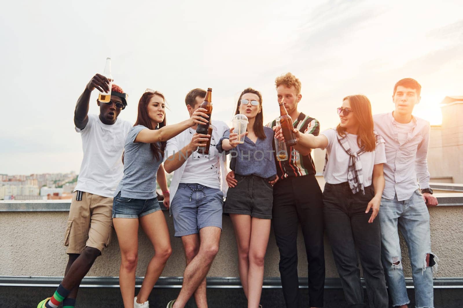 Standing with alcohol at the edge of rooftop. Group of young people in casual clothes have a party together at daytime.
